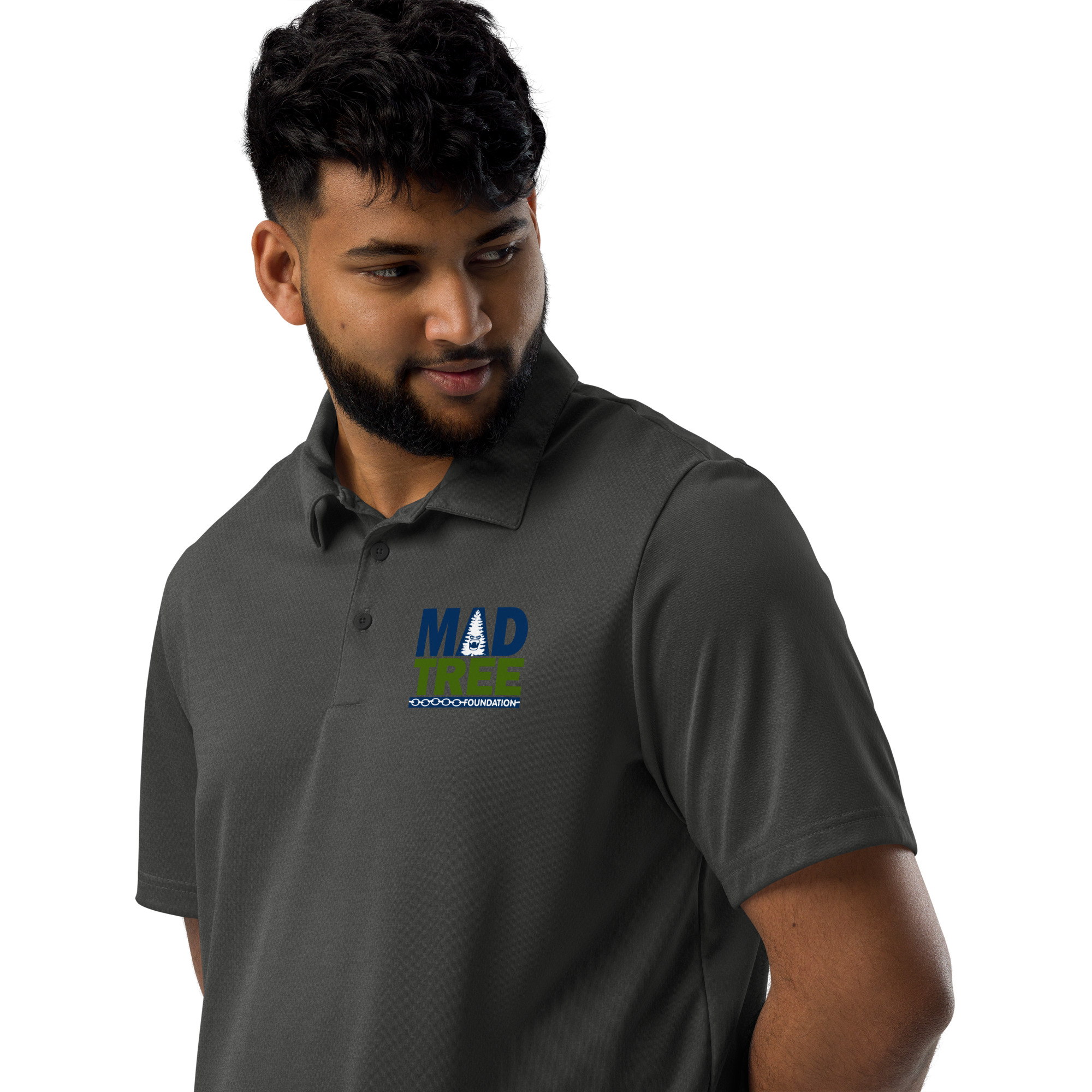 A man with short curly hair and a beard wears a dark gray adidas space-dyed polo with a blue and green MAD TREE logo on the chest, looking down and to his left against a plain white background.