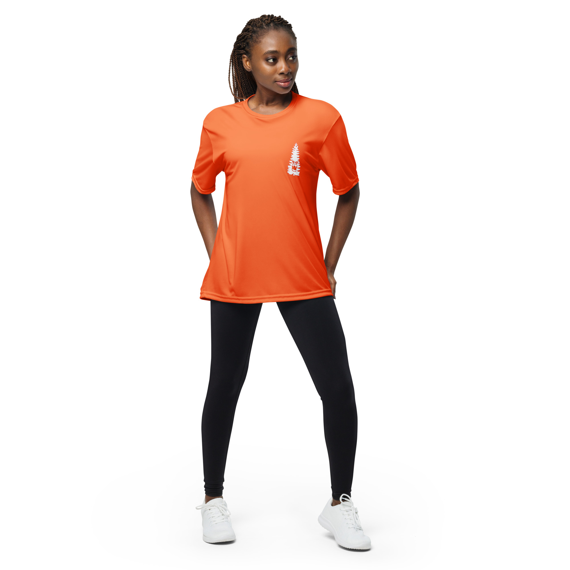 A woman stands confidently with hands in her pockets, wearing a Unisex performance crew neck t-shirt in orange with a small white graphic, paired with black leggings and white sneakers against a plain white background.