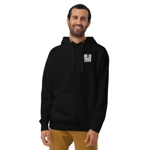 A smiling man with dark hair and a beard wears the Unisex Hoodie - Mad Tree, featuring "MAD TREE" in white text on the chest. He stands with one hand in the pocket of his tan pants.