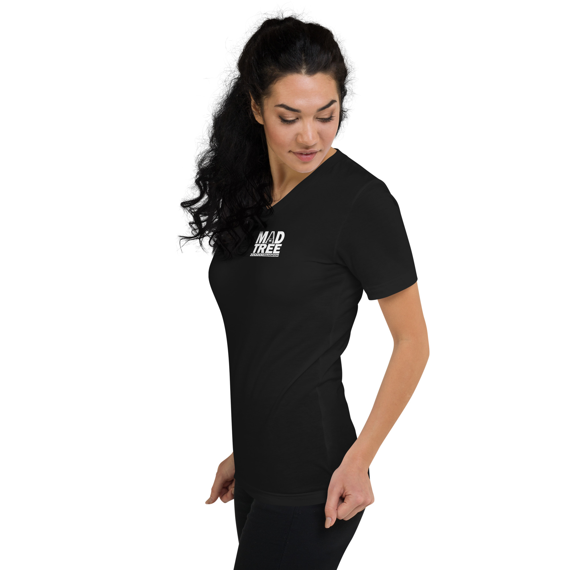 A woman with long dark hair wears the Unisex Short Sleeve V-Neck T-Shirt - Mad Tree, a fitted black shirt with "MAD TREE" in white on the chest, standing sideways and looking down against a white background.